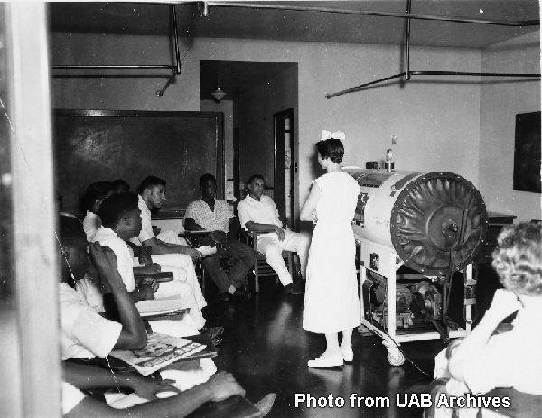 Students listen to instructor in front of an iron lung machine