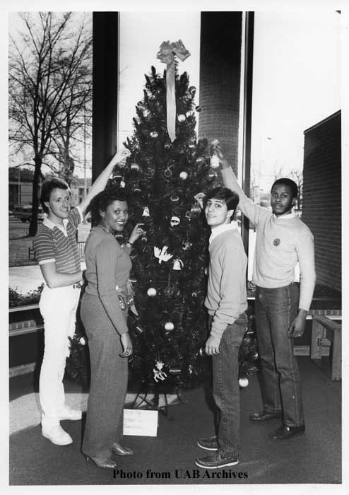 Four students stand in front a Christmas tree, reaching up