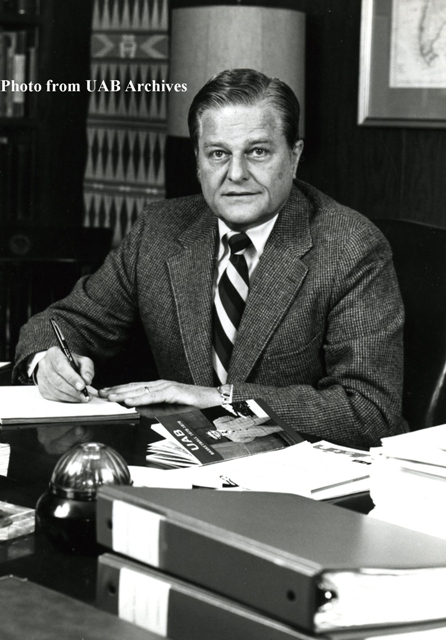 Dr. Hill sits behind a desk, signing a peice of paper