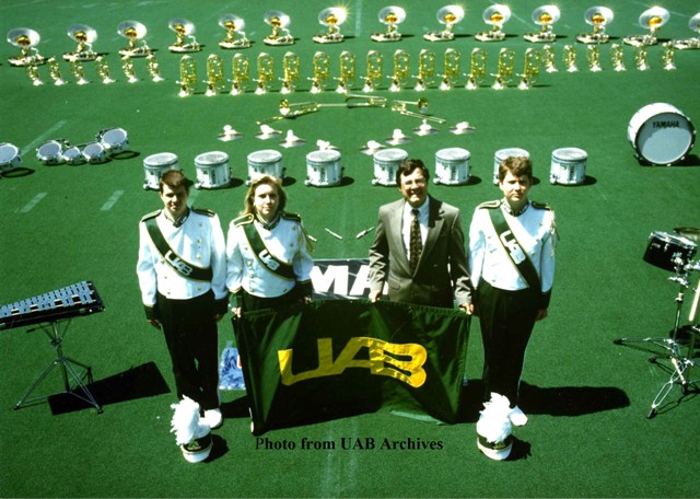 Four members of the UAB marching band stand on a field