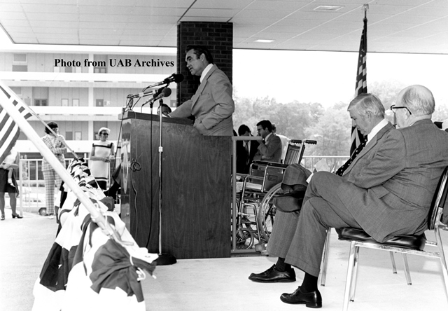 Two men watch a man address the crowd