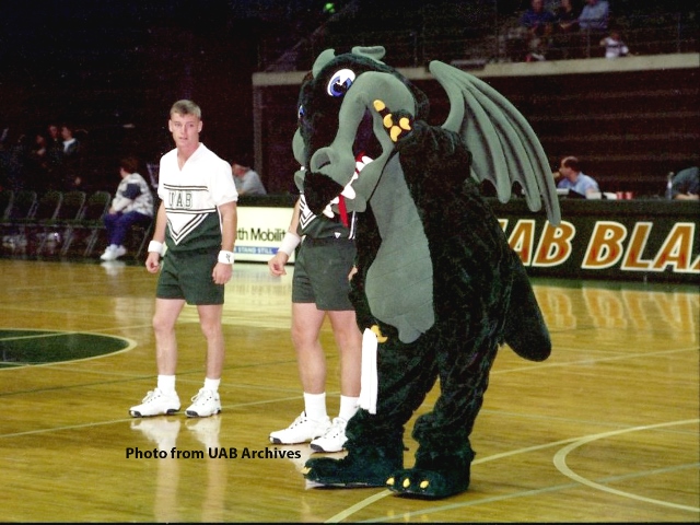 Blaze stands with two male cheerleaders on a basketball court